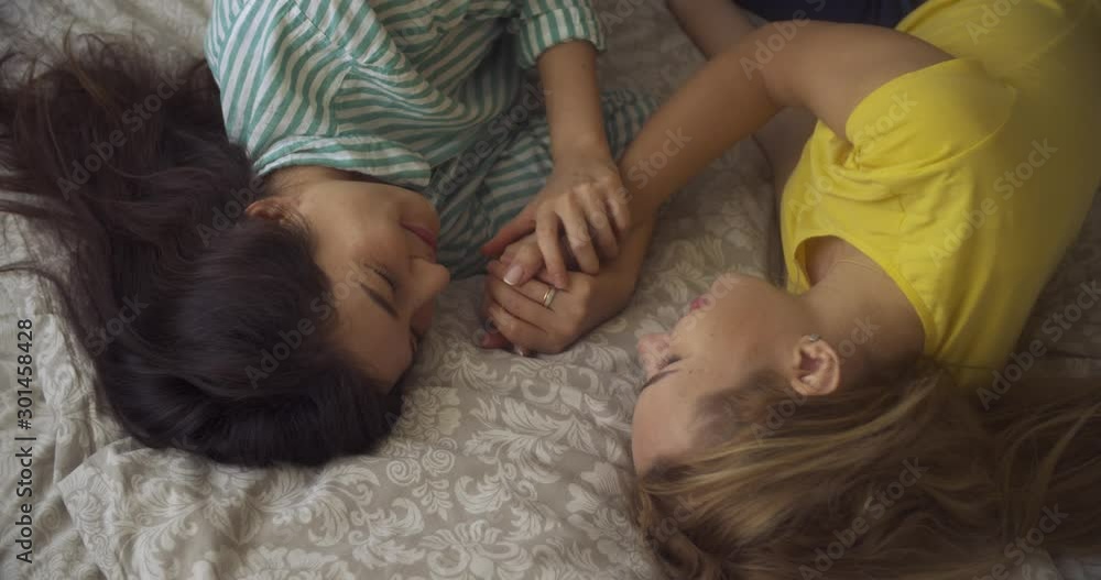 two multinational yong women lesbians lie in the bedroom on the bed and hold hands at each other. LGBT two multinational yong women lesbians lie in the bedroom on the bed and hold hands at each other. LGBT