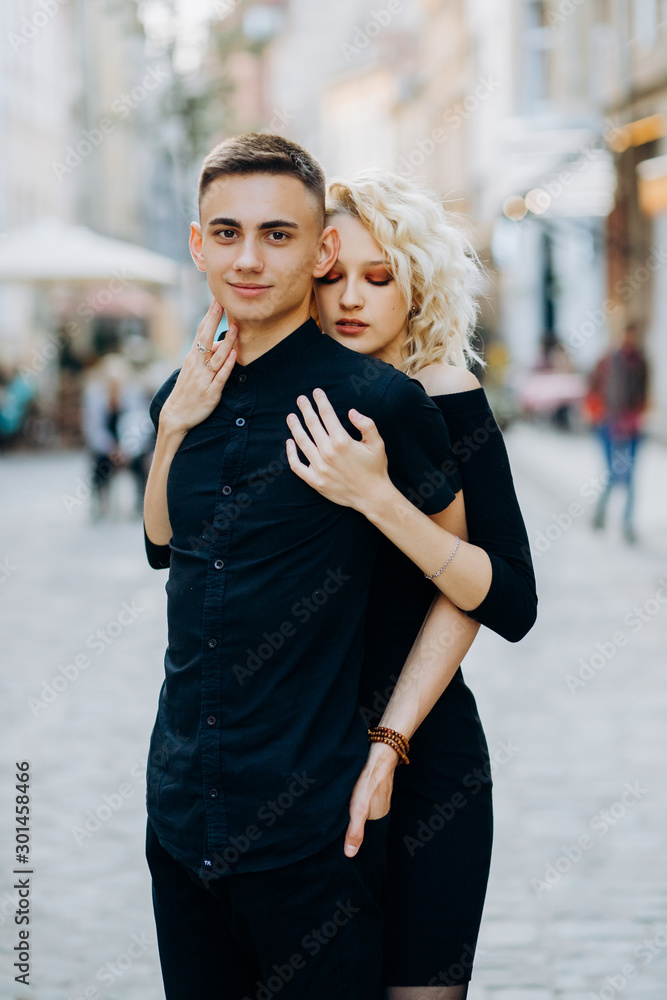 Cute blonde in a black dress hugging her boyfriend from behind