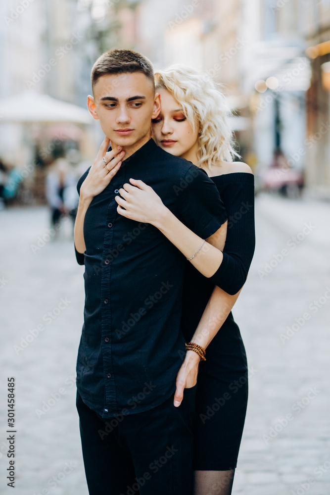 Lovely blonde in a black dress hugging her boyfriend from behind Lovely blonde in a black dress hugging her boyfriend from behind