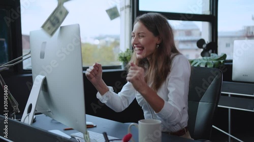 Young successful woman typing keyboard at desktop computer winning lottery overjoyed with financial success business profits and money rain. Rich people.