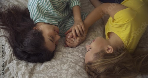 two multinational yong women lesbians lie in the bedroom on the bed and hold hands at each other. LGBT
