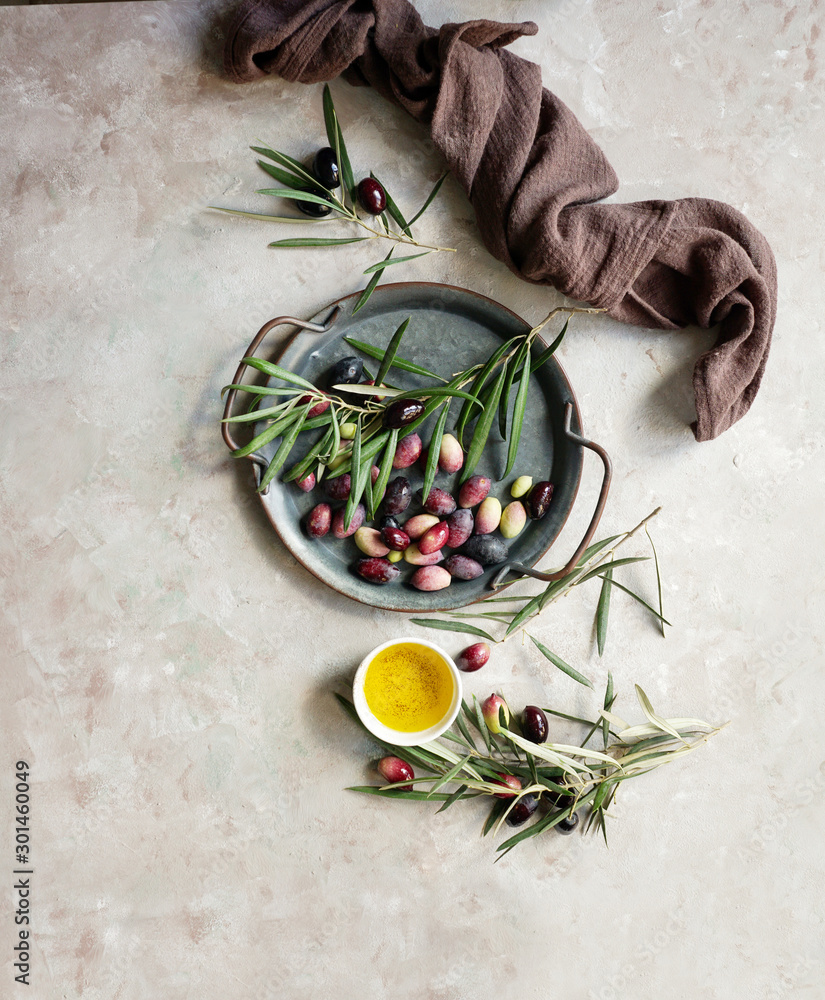 Food background with olive tree branch, napkin and plate, knife and fork cutlery, olive oil on concrete background Food background with olive tree branch, napkin and plate, knife and fork cutlery, olive oil on concrete background
