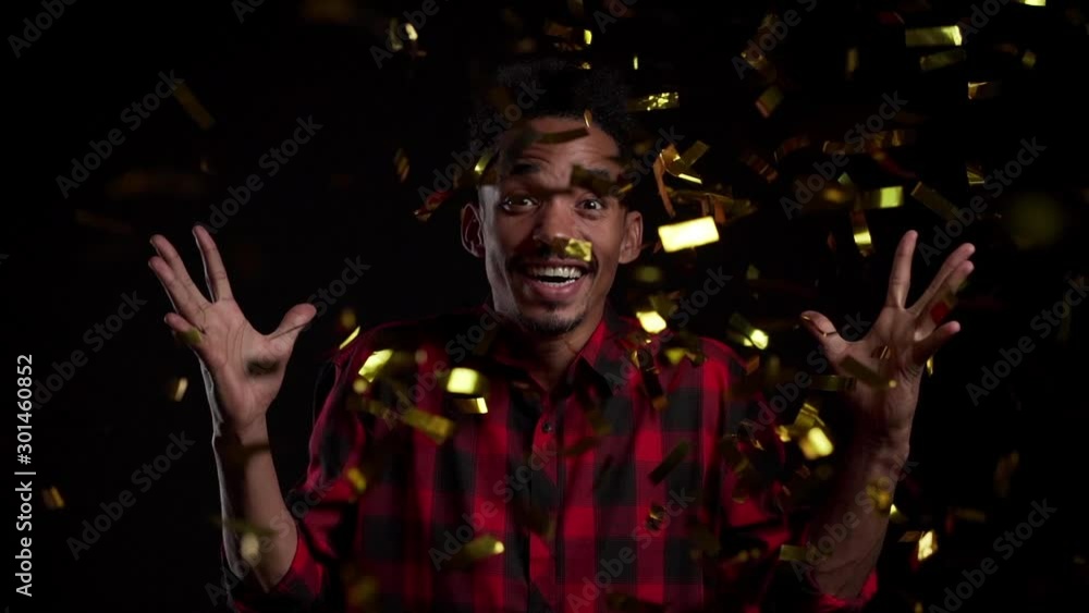Surprised excited african man winning, having fun in confetti rain on black background. Guy celebrating, depicts joy and happiness. Success, victory, holiday concept. Surprised excited african man winning, having fun in confetti rain on black background. Guy celebrating, depicts joy and happiness. Success, victory, holiday concept.