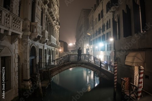 Lovers on a bridge at night in a foggy Venice