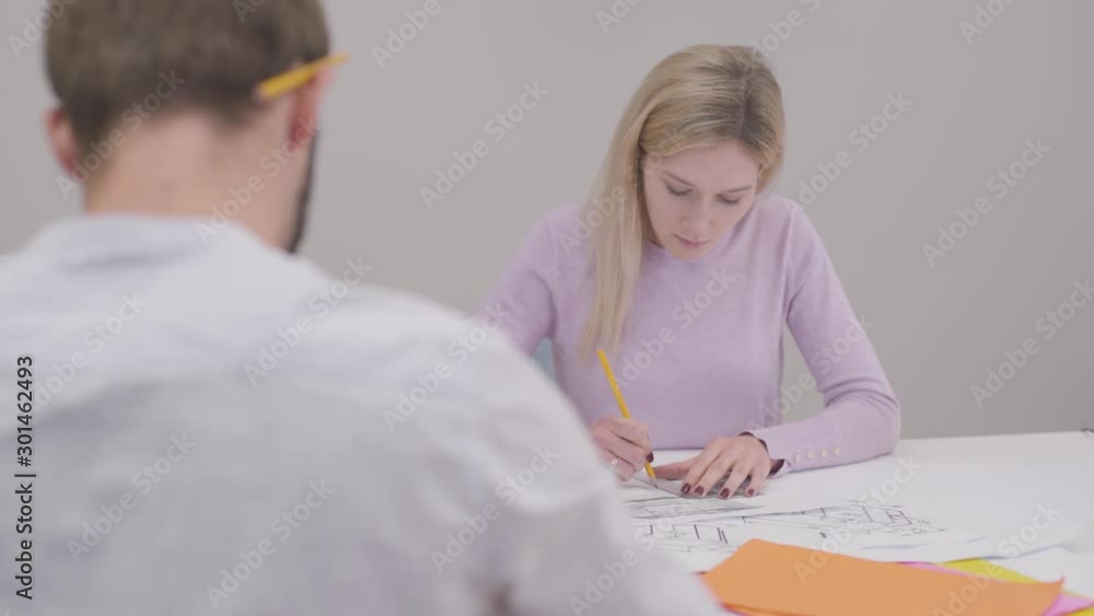 Young exhausted Caucasian woman drawing blueprint, striking out mistake and holding her head with hand. Professional designer working in the office. Specialist implementing ideas on paper. Young exhausted Caucasian woman drawing blueprint, striking out mistake and holding her head with hand. Professional designer working in the office. Specialist implementing ideas on paper.