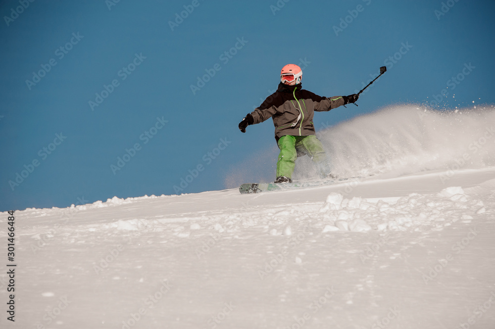 Man riding down the hill on the snowboard with the camera in hands