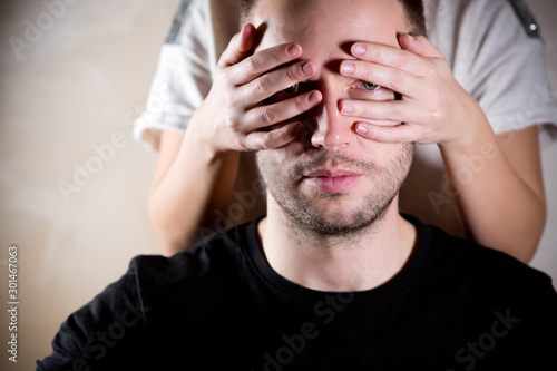 the woman closes the eyes of the man with her palms  but he can look through her fingers