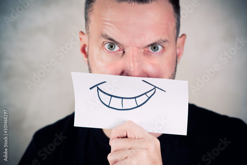 angry man covers his mouth with a sheet with a painted smile. close up