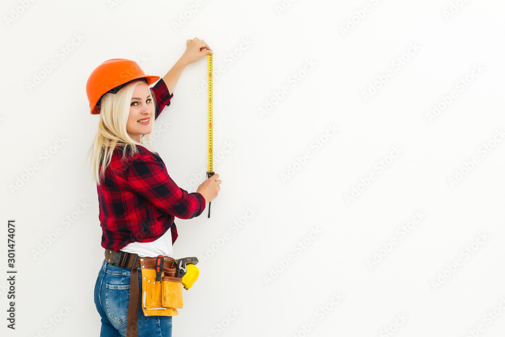 Woman builder in uniform measuring wall with tape Woman builder in uniform measuring wall with tape