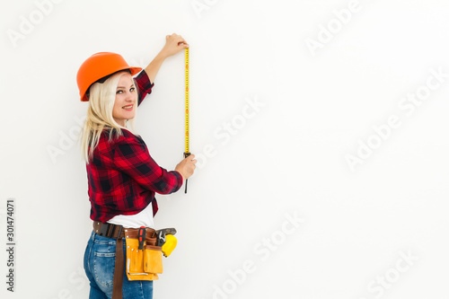 Woman builder in uniform measuring wall with tape