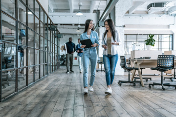 Sharing fresh office news. Two young colleagues in smart casual wear discussing business and smiling while walking through the office