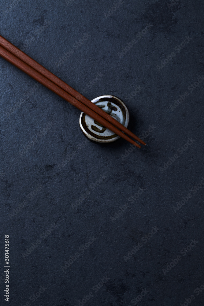 Wooden chopsticks and chopstick rest on dark stone background. Top view. Copy space. Wooden chopsticks and chopstick rest on dark stone background. Top view. Copy space.