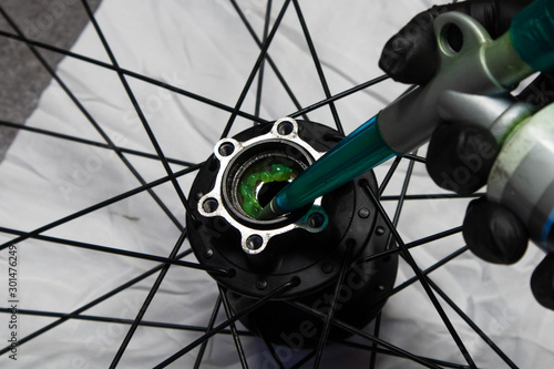 Close up photo of a bicycle mechanic's hand wearing a black latex glove greasing a bicycle rear hub. 