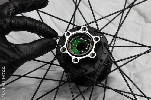 Close up photo of a bicycle mechanic's hand wearing a black latex glove inserting bearing balls into the hub.
