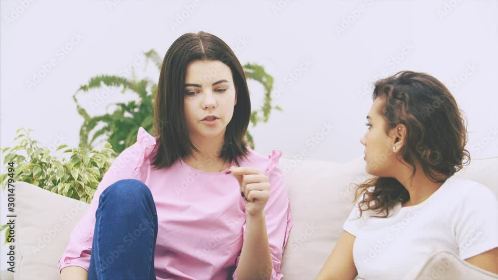 Cute caucasian girl is telling her afro-american friend a story, looking serious, gesturing emotionaly.