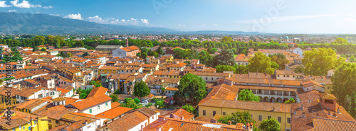 Aerial top panoramic view of historical centre medieval town Lucca with old buildings, typical orange terracotta tiled roofs and mountain range, hills, blue sky white clouds background, Tuscany, Italy