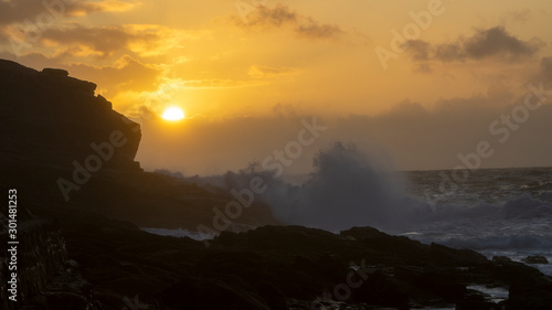 As the sunsets waves crash onto  Rocks near Sennen Harbour  Atlantic Ocean Cornwall West Country England UK United Kingdom GB