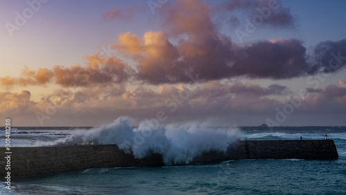 As the sunsets waves crash onto Rocks near Sennen Harbour, Atlantic Ocean Cornwall West Country England UK United Kingdom GB