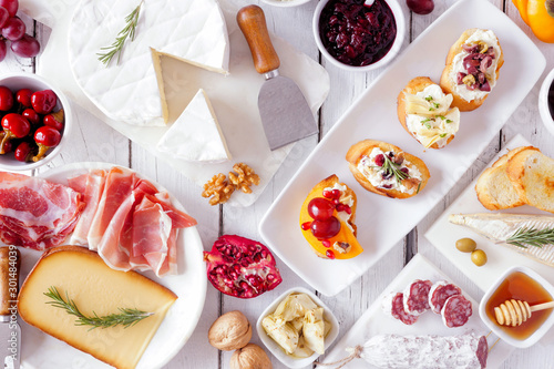 Party appetizers of assorted cheeses, meats and crostini. Top view on a white wood background.