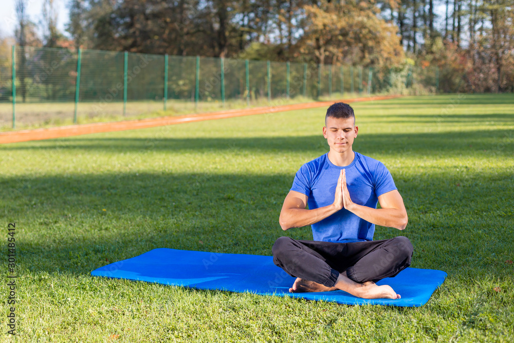 Young man wearing athletic wear sitting in the park exercising yoga Young man wearing athletic wear sitting in the park exercising yoga