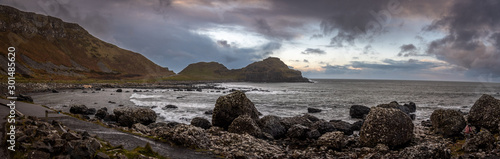 Panoramic view of the pathways and the bay at the coast called Giant's Causeway, a landmark in Northern Ireland, with the cliffs that surround the place and dramatic cloudy sky.