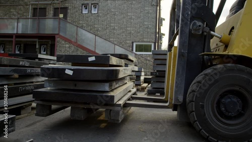 View of yellow forklift pallets lifter heavily loaded with dark granite blocks is lifting them up at outside area of some warehouse. photo