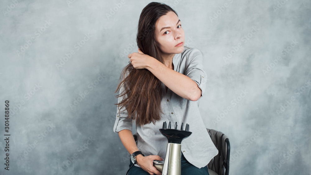 A young woman with long dark hair uses a hair dryer to dry and style. Hairstyle styling and hair care,