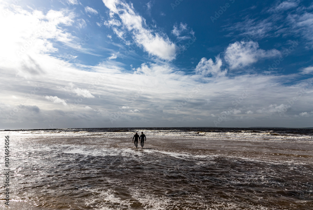 Two men in the distance wet suits going into the ocean, stormy skies background