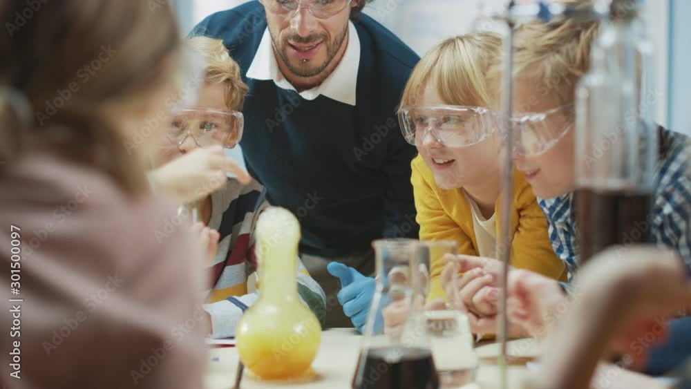 Elementary School Science Classroom: Enthusiastic Teacher Explains Chemistry to Diverse Group of Children, Little Boy Mixes Chemicals in Beakers. Children Learn with Interest Elementary School Science Classroom: Enthusiastic Teacher Explains Chemistry to Diverse Group of Children, Little Boy Mixes Chemicals in Beakers. Children Learn with Interest