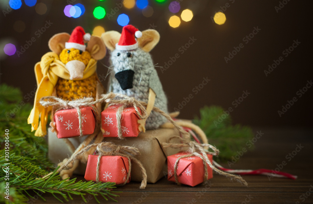 Rats knitted from yarn in Christmas caps. Gift boxes, spruce branches and Christmas garland.
