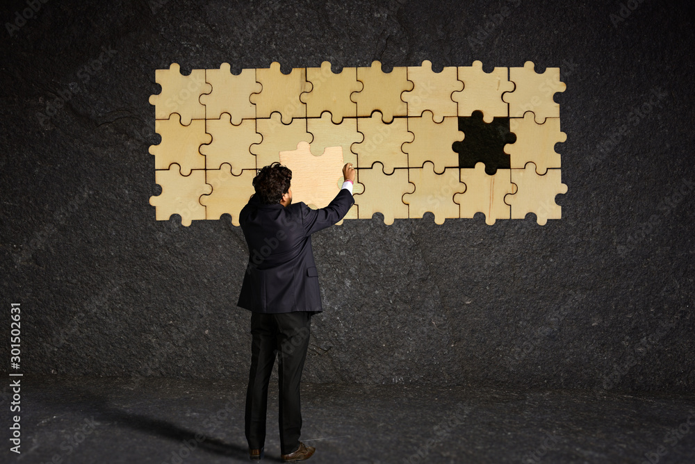 Businessman try to complete puzzle on the wall with puzzle pieces Businessman try to complete puzzle on the wall with puzzle pieces