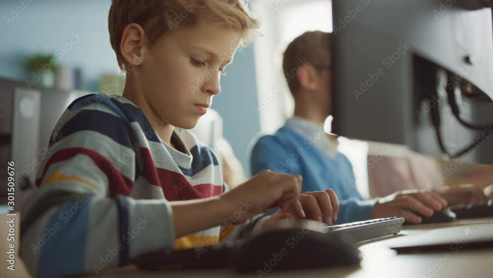 Elementary School Computer Science Classroom: Smart Little Boy Uses Personal Computer, Learning How to Use Internet Safely, Programming Language for Software Coding. Modern Education. Portrait View Elementary School Computer Science Classroom: Smart Little Boy Uses Personal Computer, Learning How to Use Internet Safely, Programming Language for Software Coding. Modern Education. Portrait View