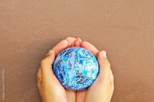A small globe on the palm Brown wall background.Blue small world on two hands Brown wall background Free space above All around.copy space