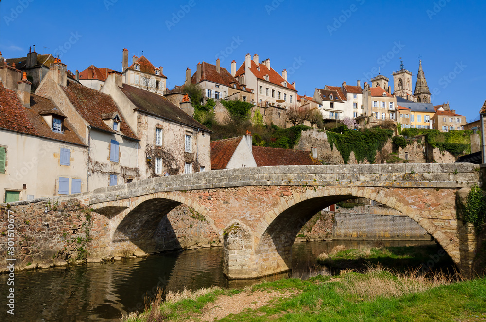 Stone bridge over the river in the old French town. On the mountain there are traditional houses with tiled roofs and a church. Semur-en-Osois, Burgundy, France