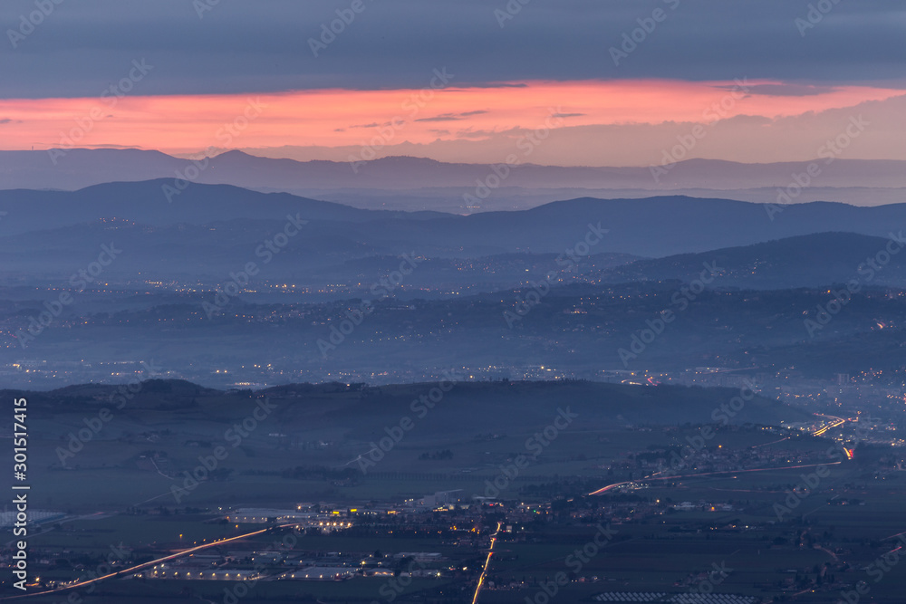 A view of Umbria valley at dusk with hills, mist and city lights