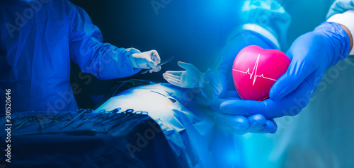 Double exposure Several surgeons surrounding patient on operation table during their work and Doctor or surgeon holding a Heart.Doctor hands holding red heart with cardiogram, health care concept.