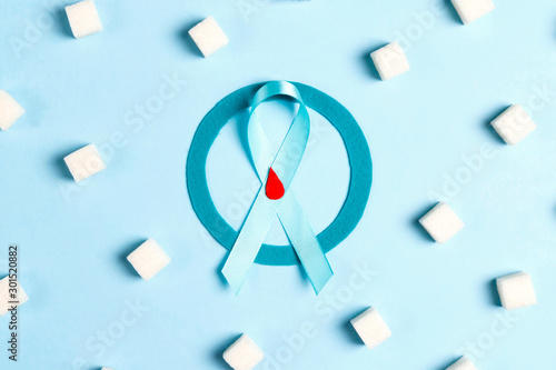 Blue circle with ribbon and drop of blood as a symbol of diabetes surrounded by sugar on a blue background. photo