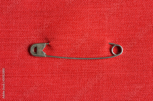 Silver color safety pin attached to red fabric background. Closeup. Copy space