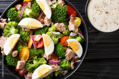 Breakfast salad with tuna, broccoli, tomatoes, onions and eggs and yogurt dressing closeup in a plate. Horizontal top view