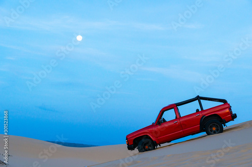 A red jeep on the white sand dune in an early morning with the moon, Muine, Vietnam