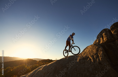Wallpaper Mural Silhouette of professional bicyclist balancing on trial bicycle on top of big boulder, male rider making acrobatic stunt on summer evening, blue sky and sunset on background. Concept of extreme sport Torontodigital.ca