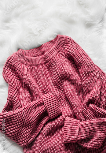 Color raspberry woolen women's sweater on a white fluffy carpet, top view. Fashion concept
