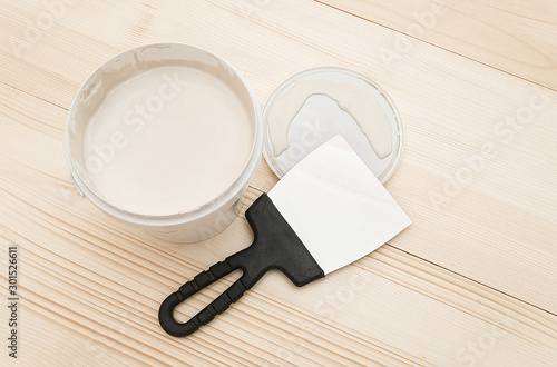 Spatula and a bucket of white putty on wooden boards. Top view Copy space