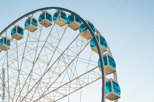 White ferris wheel with blue booths on the background of a blue sky. Amusement park.