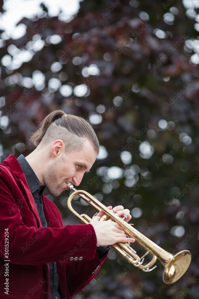 Obraz premium young handsome trumpeter playing jazz on his gold trumpet in autumnal park 