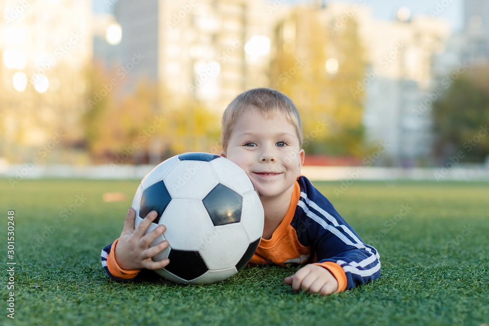little boy sitting on a football field with a soccer ball