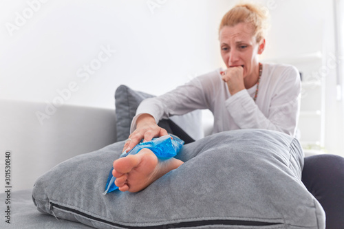 Injured woman holding ice pack / bag for cooling down the ankle pain.