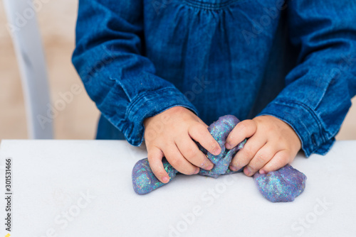 Child crumples slime. Close up of hands. Process of making slime. Blue magic glitter slime on a white background.