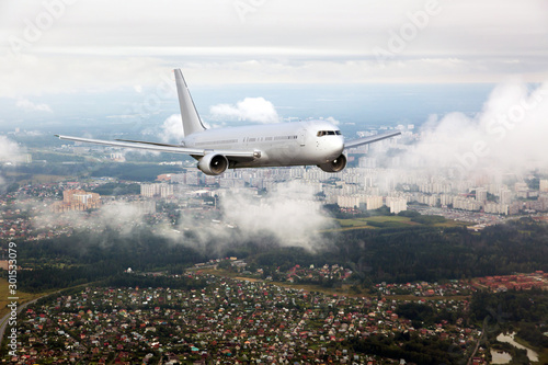 Passenger plane in flight. Aircraft flyes through the clouds above the buildings of city quarters.