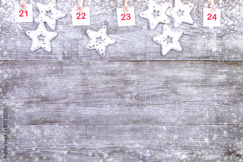21-24 part of Advent calendar with sheets with numbers and christmas toys stars on white wooden snowy background.